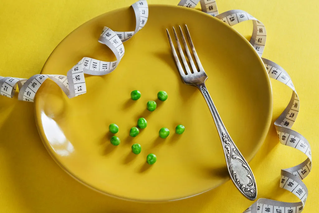 An empty plate with a couple of peas on and a tape measure