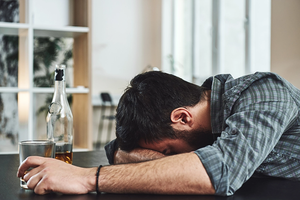 A man passed out at the bar with a bottle of liquor suffering from alcohol withdrawal